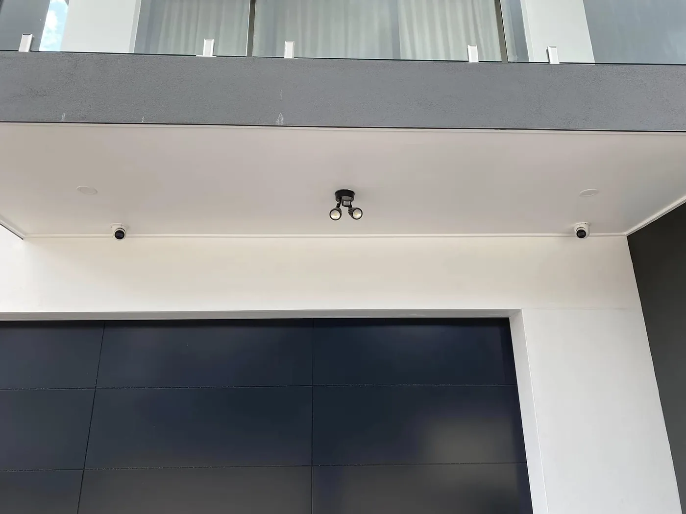 Two dome security cameras and a floodlight above a garage door