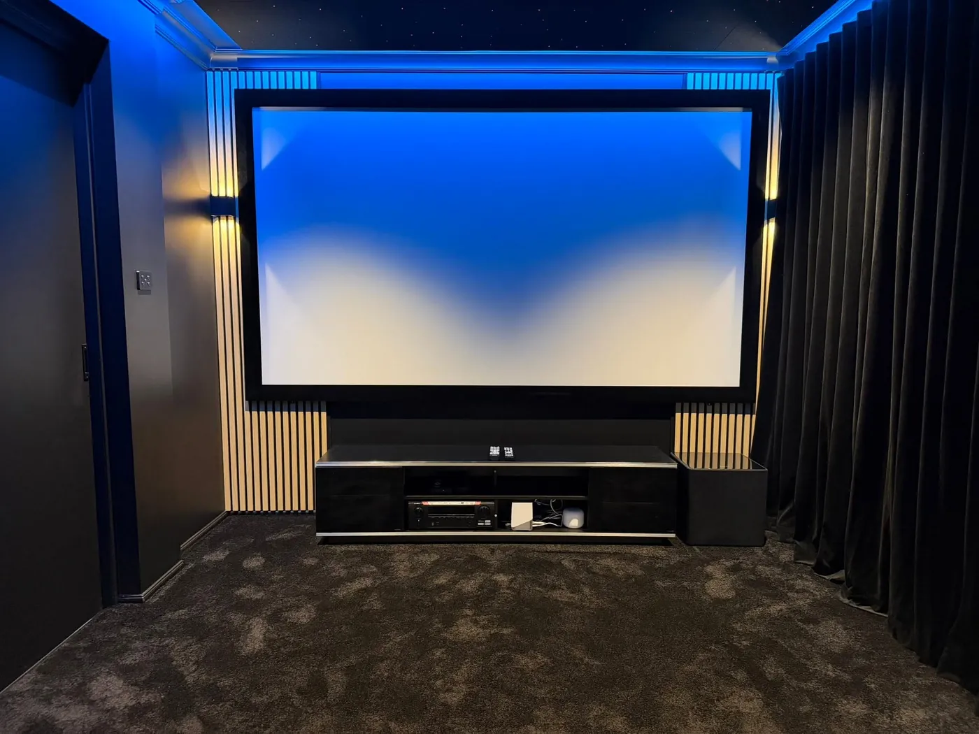 Finished cinema room with a slatted screen wall, blackout curtains and blue LED lighting