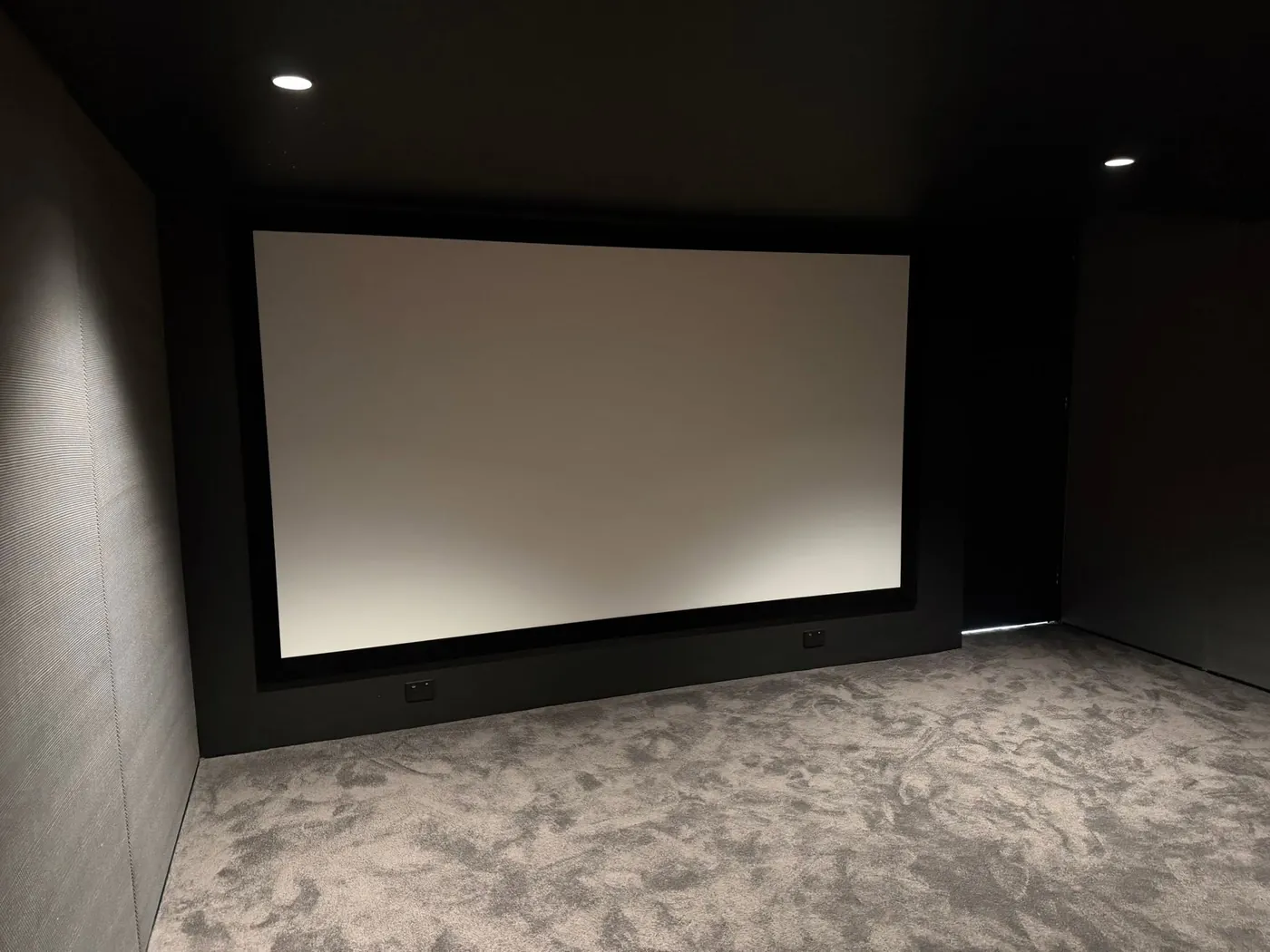 Finished dark cinema room with a large projection screen and grey carpet