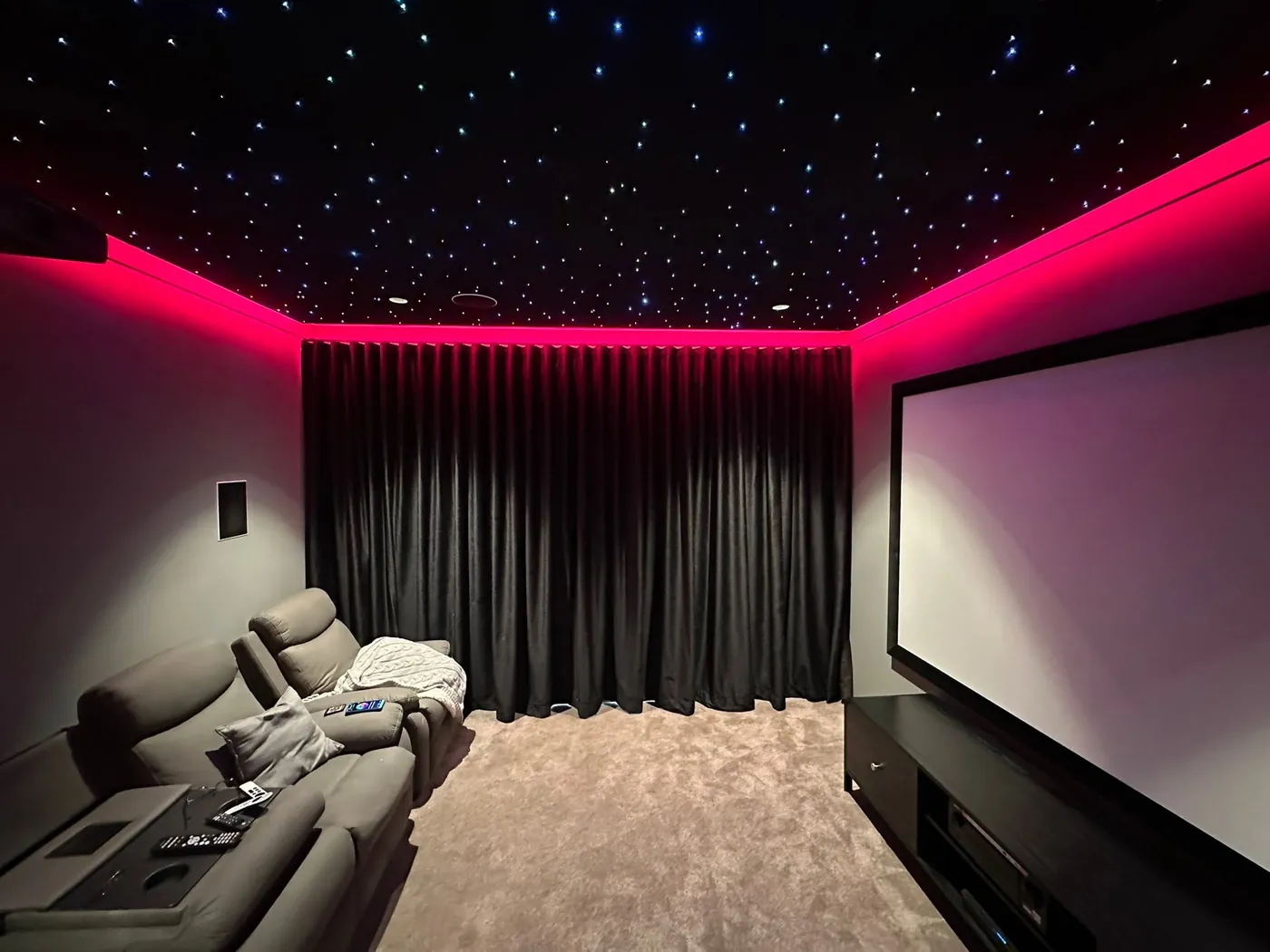 Finished cinema room with a projection screen, star-light ceiling, red LED lighting and curtains