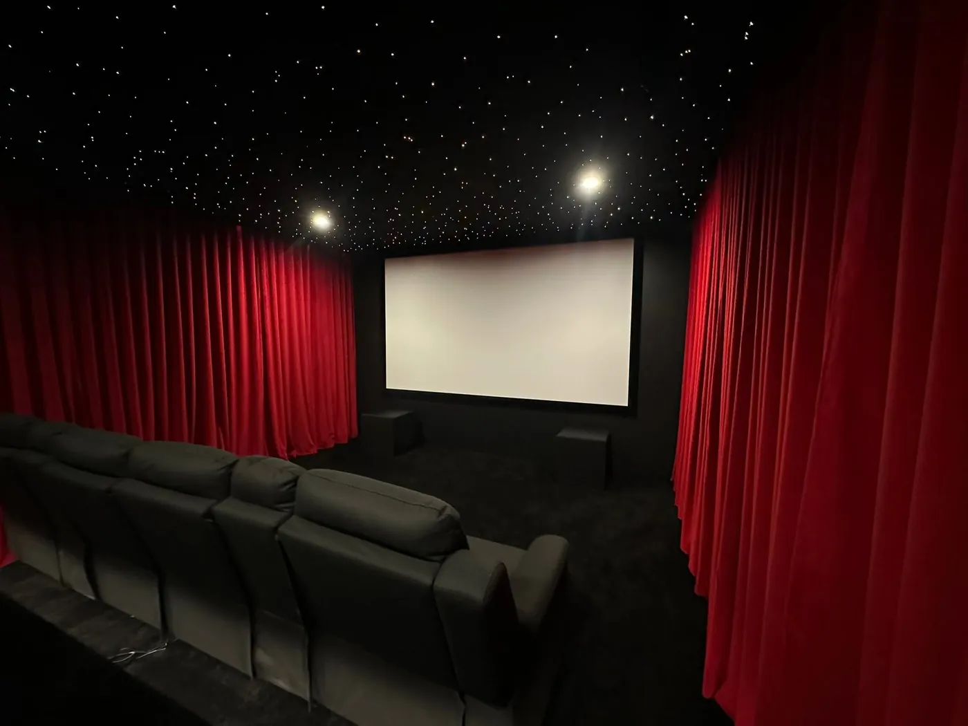 Finished cinema room with a star-light ceiling, red velvet curtains and a row of recliners