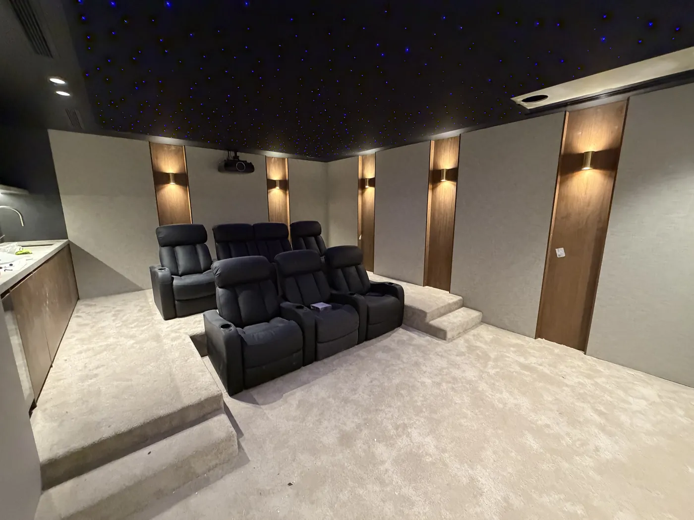 Cinema room with timber panel wall sconces, a star-light ceiling and tiered recliners