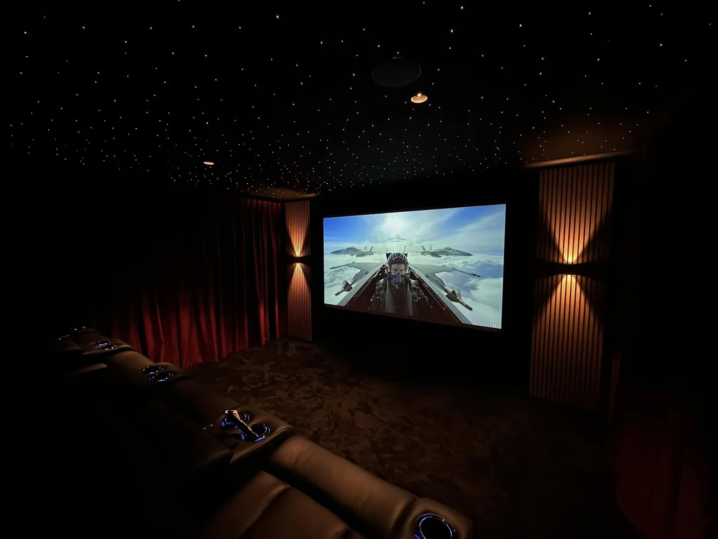 Wall sconces and a star-light ceiling above recliners facing the screen