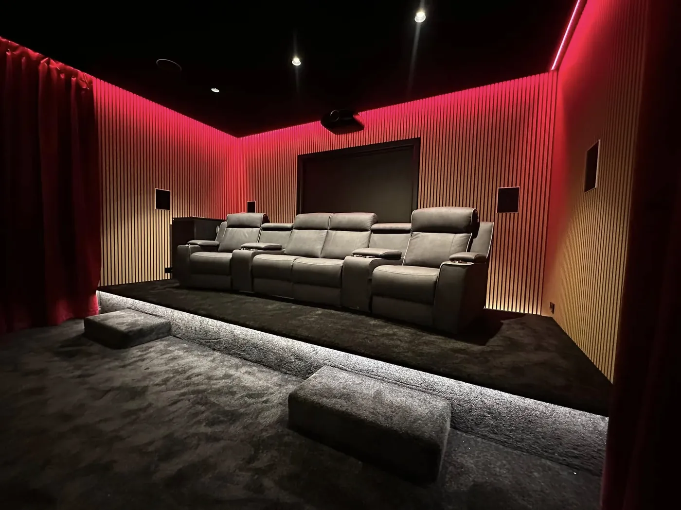 Grey leather recliners on a lit riser with red LED lighting and timber slat walls