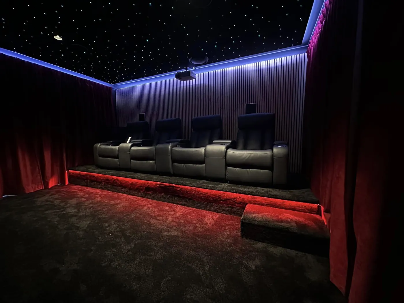 Row of black leather recliners on a riser with red LED lighting and velvet curtains