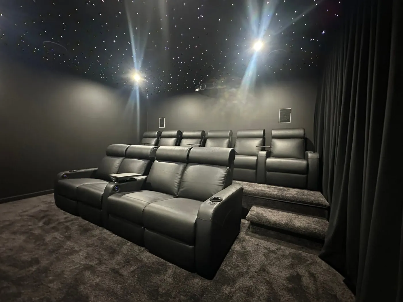 Two tiers of black leather recliners under a star-light ceiling