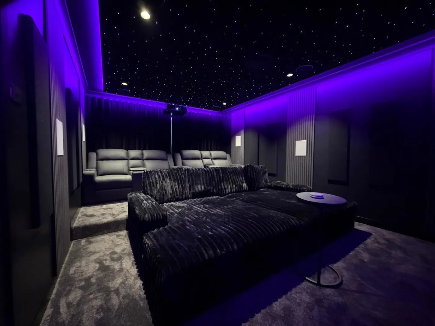Black lounge bed in front of a row of recliners under purple LED lighting