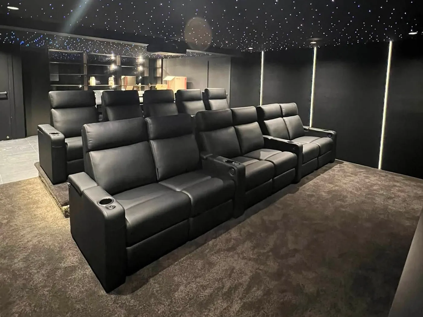 Two rows of black leather recliners under a star-light ceiling