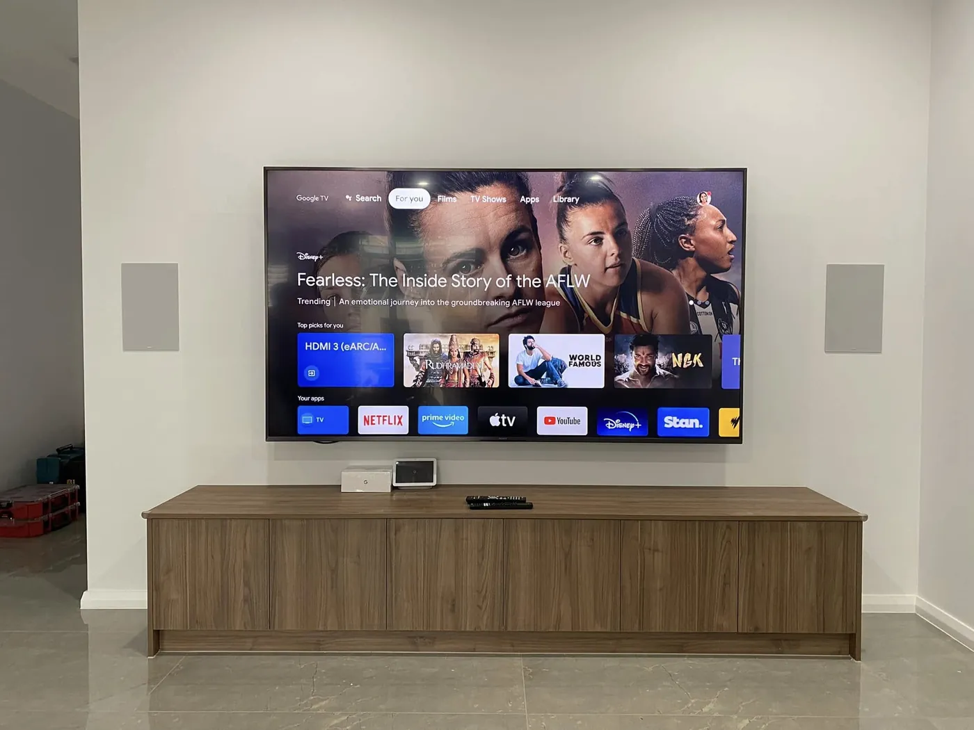 Large TV wall-mounted above a timber cabinet with in-wall speakers either side