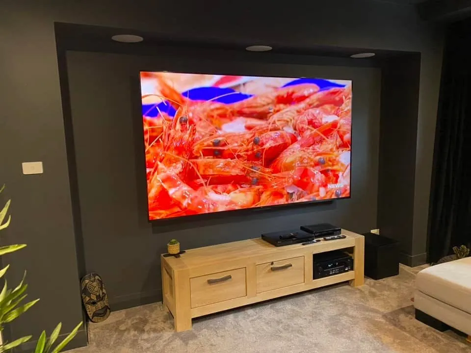 Large TV mounted on a dark feature wall above a timber cabinet