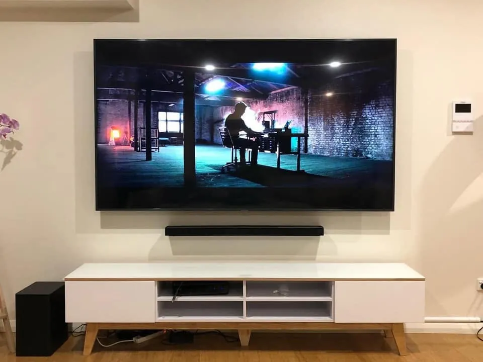 TV wall-mounted above a soundbar and a white cabinet